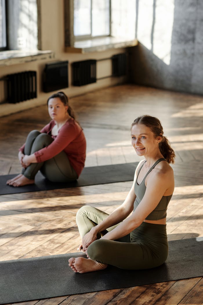 Two women sitting on yoga mats in a sunlit studio, embracing relaxation and mindfulness.