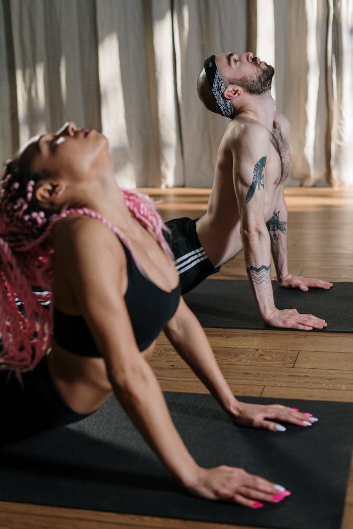Two individuals practicing yoga indoors, highlighting strength and flexibility in a sunlit studio.